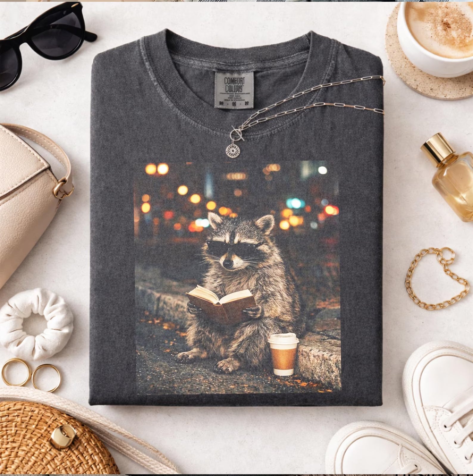 Reading Raccoon graphic tee from Anchored Grace Boutique featuring a cute raccoon reading a book on soft fabric.
