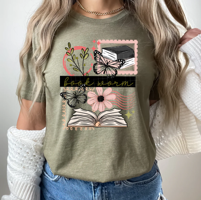 Graphic tee featuring Book Worm Stamps design from Anchored Grace Boutique, with colorful book and stamp illustrations.