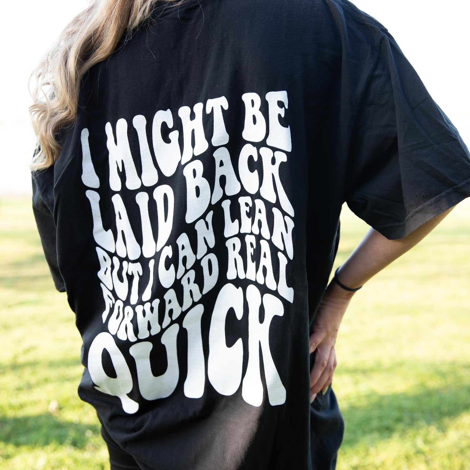 Black graphic tee by Shop Karma Tees with "I Might Be Laid Back" slogan and casual fit, displayed on a hanger.