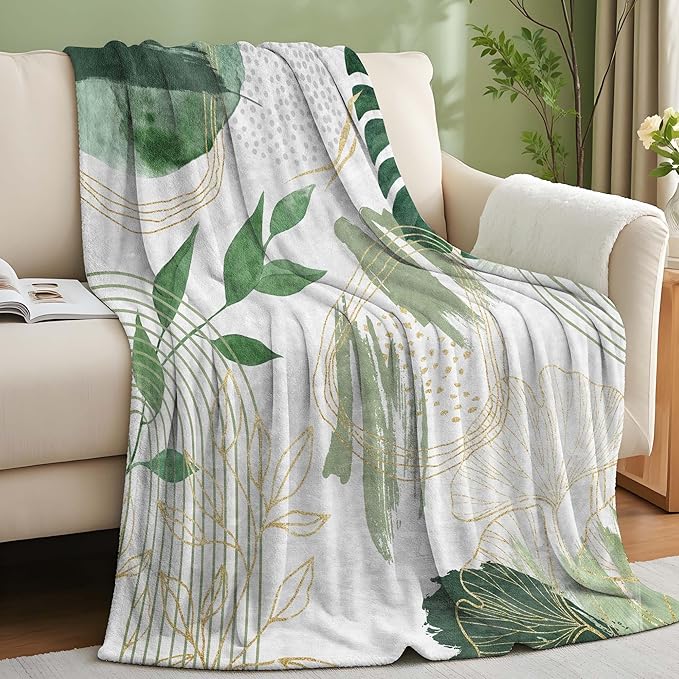 Sage green leaf throw blanket by CozyNest Decor with gold accents, soft flannel, mid-century boho style, 50x60 inches on a sofa.