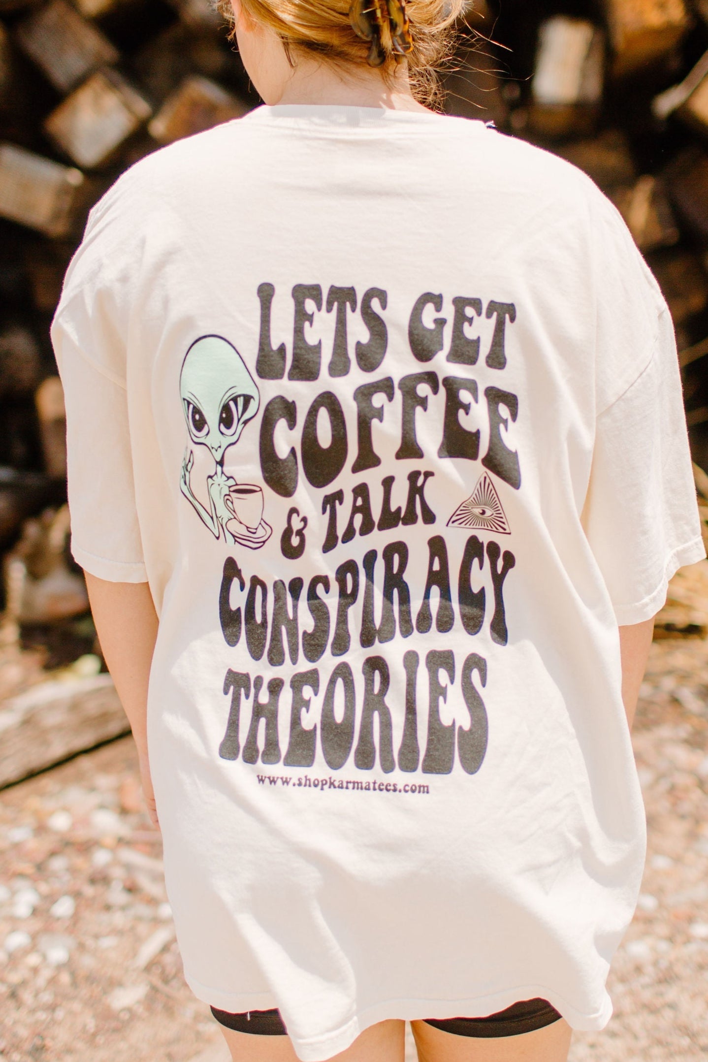 Black graphic tee from Shop Karma Tees featuring coffee cups and conspiracy theory illustrations on the front.