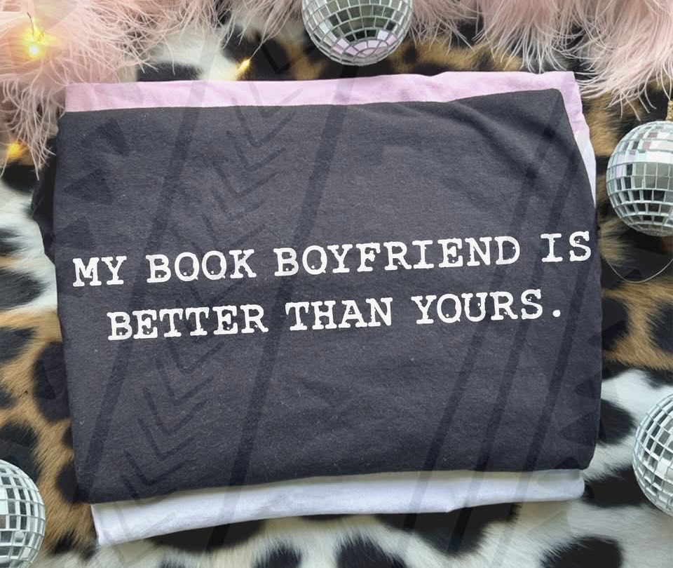 Black graphic tee with "My Book Boyfriend is Better Than Yours" quote from Anchored Grace Boutique, casual wear for book lovers.
