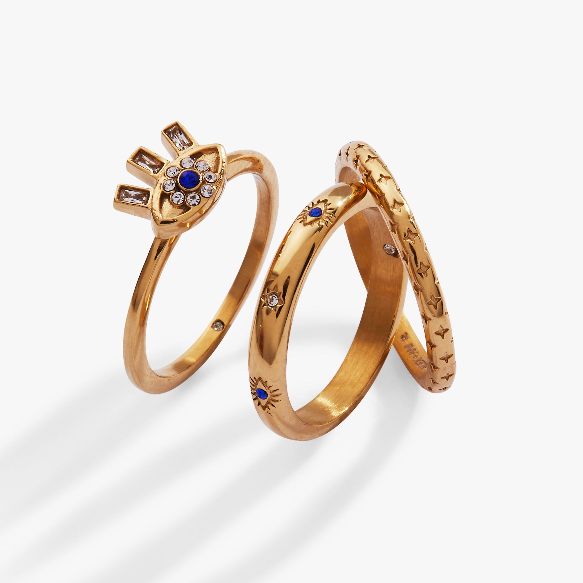 Set of three gold stainless steel evil eye stacking rings by ALEX AND ANI, featuring detailed eye designs and smooth band finishes.