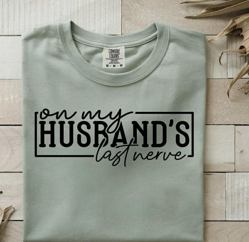 On My Husband's Last Nerve graphic tee by Anchored Grace Boutique, featuring humorous text on a casual cotton t-shirt.