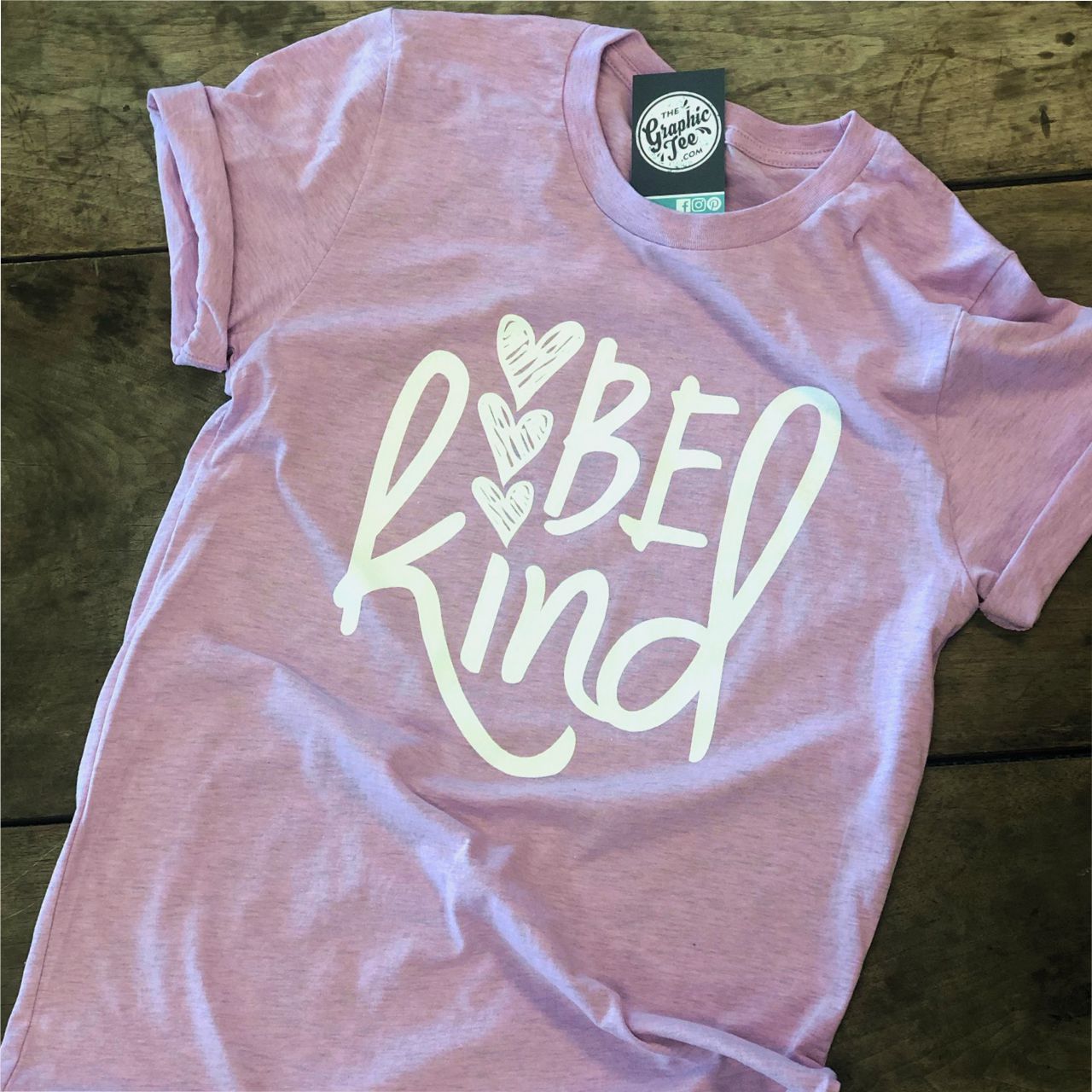 Lilac short-sleeve graphic T-shirt by The Graphic Tee with "Be Kind" slogan in stylish white font.