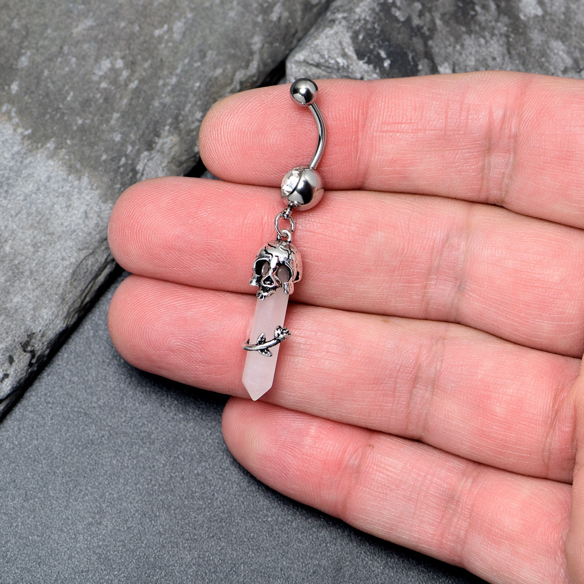 Pink Rose Quartz Skull Obelisk dangle belly ring from BodyCandy featuring a rose quartz skull design and dangling rose accents.
