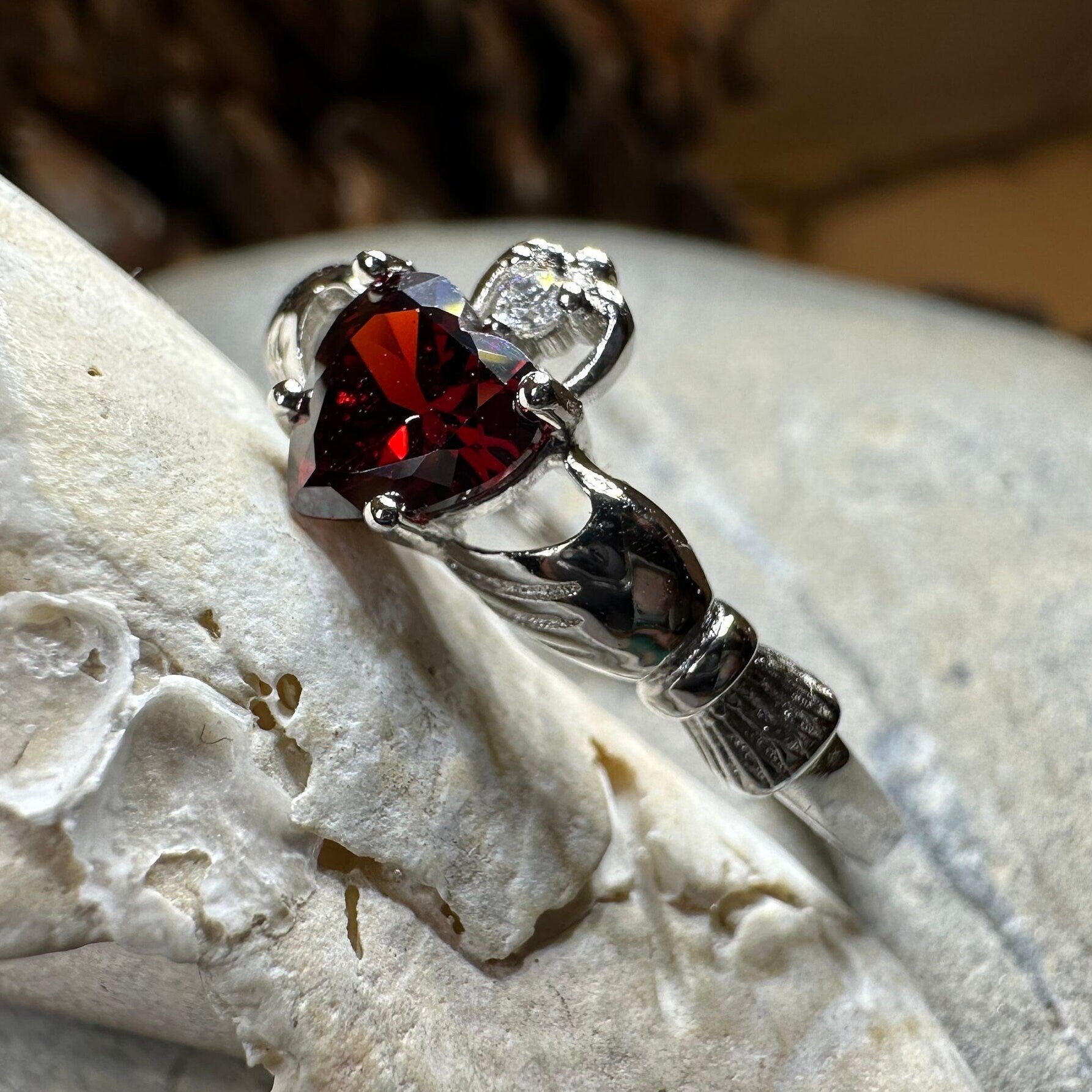 Celtic Crystal Design Jewelry Garnet Claddagh Ring showing a detailed gold band with a heart and crown motif featuring a deep red garnet gemstone.