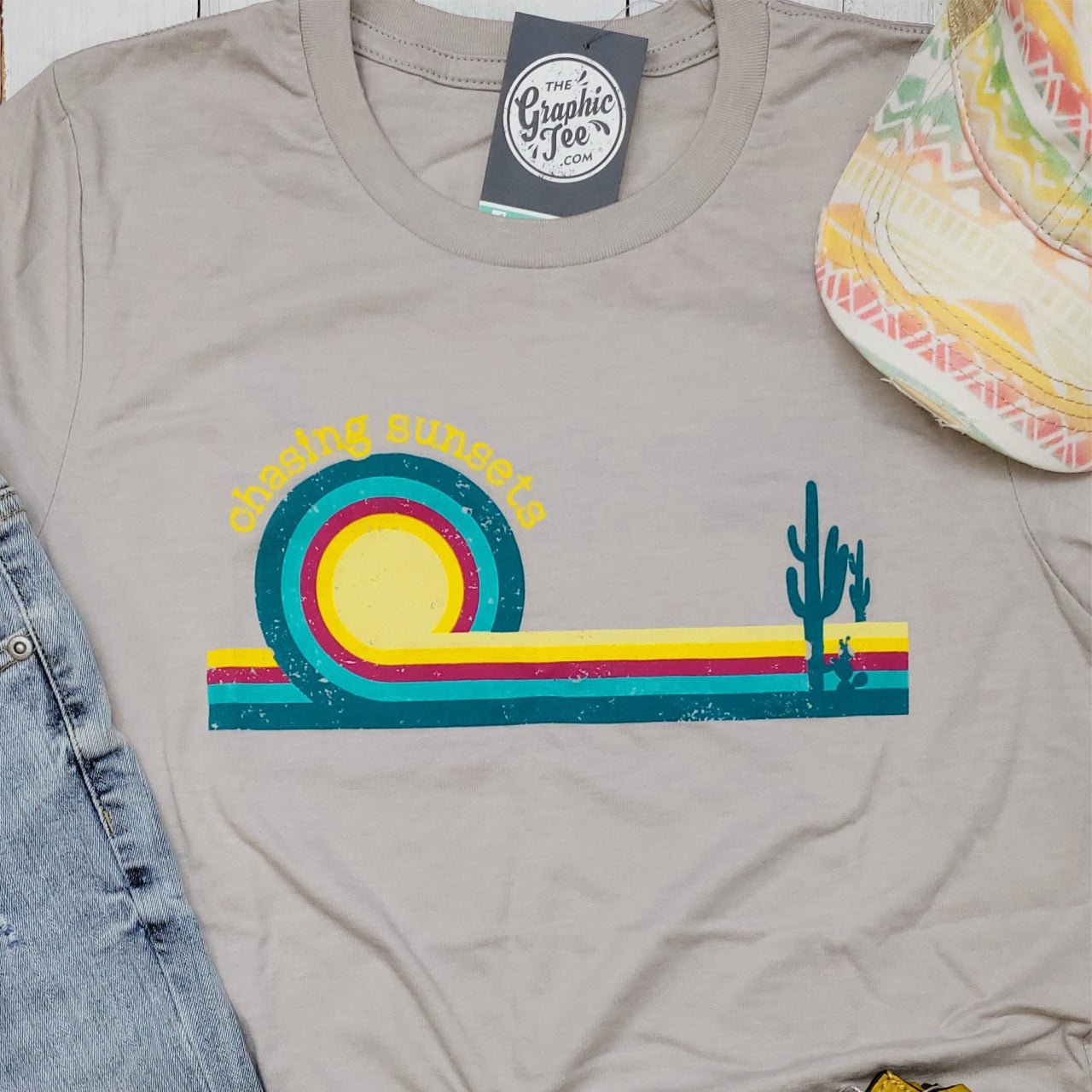 The Graphic Tee Chasing Sunsets retro graphic short sleeve t-shirt with sunset design on white fabric.