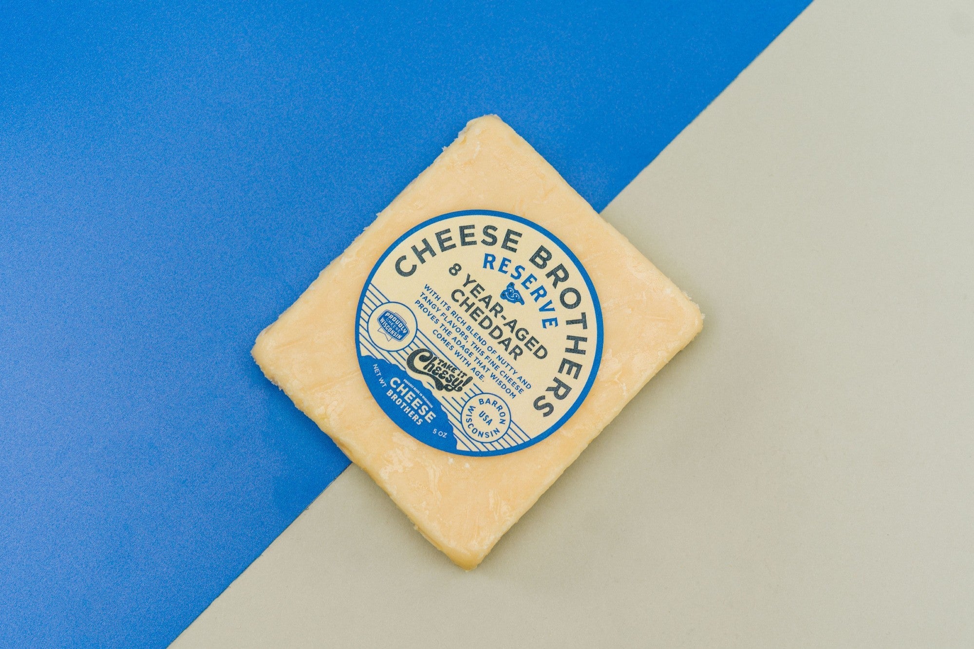 A block of 8-year-aged cheddar cheese from Cheese Brothers, Inc., showcasing its firm texture and rich, golden color.