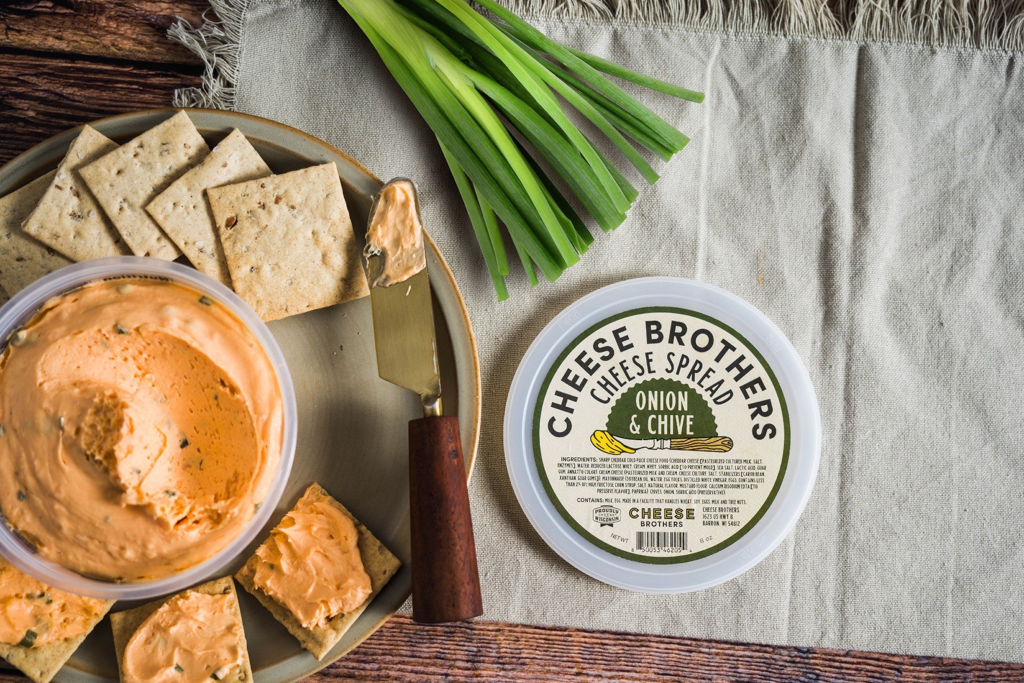 Creamy onion and chive cheese spread by Cheese Brothers Inc. with visible chopped onions and chives on a spreadable surface.