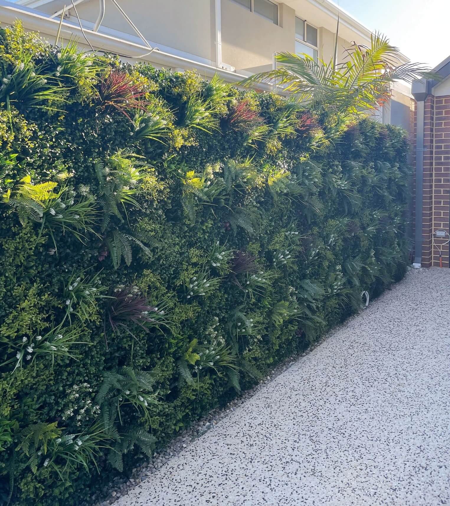Artificial green wall panel by Designer Plants USA, UV resistant living wall panel installed on dividing fence.