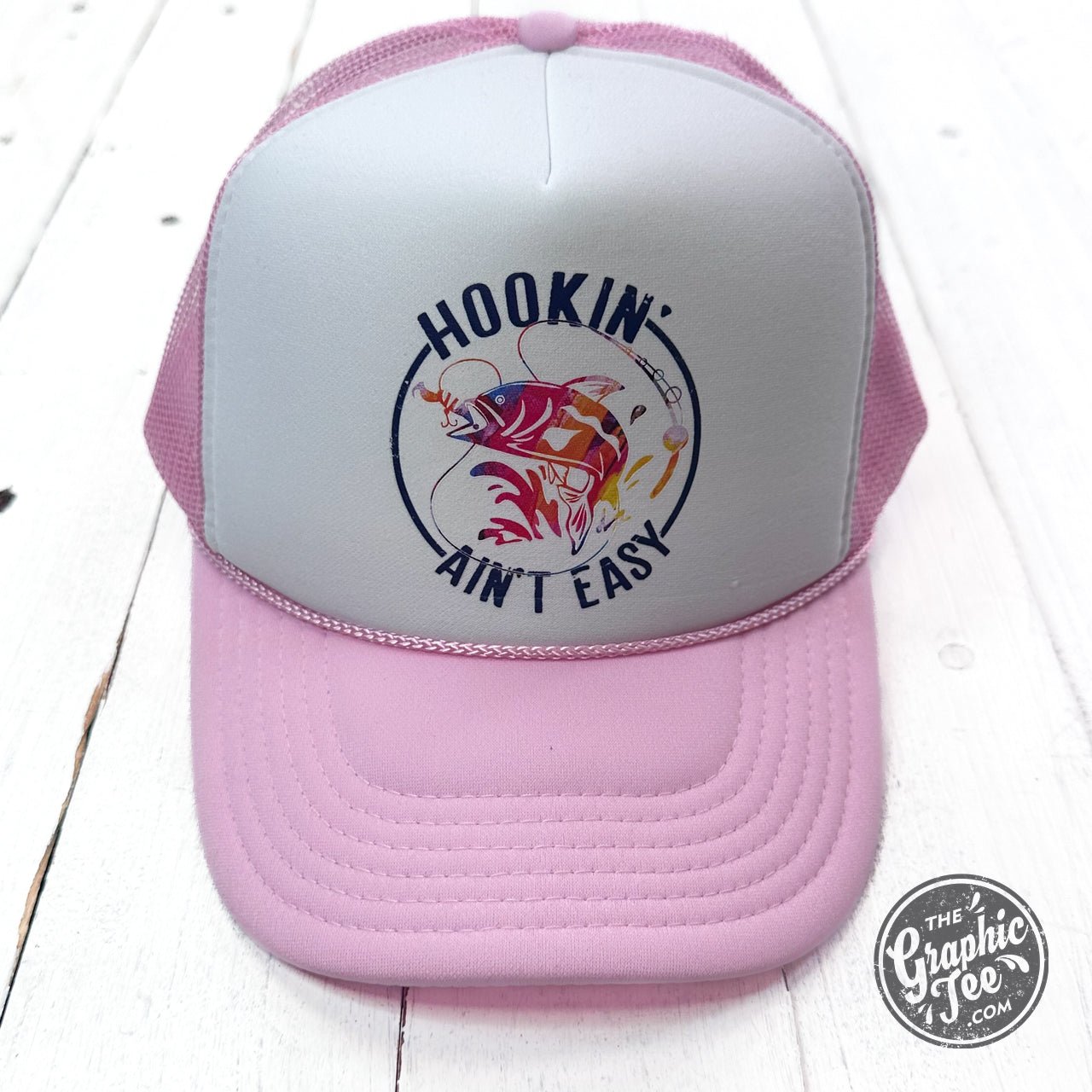 Foam trucker cap branded The Graphic Tee with "Hookin' Ain't Easy" slogan, featuring a structured front panel and mesh back.