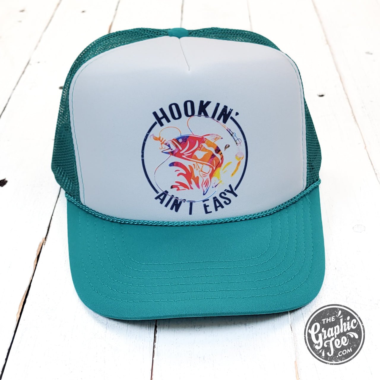 Foam trucker cap with "Hookin' Ain't Easy" graphic from The Graphic Tee, featuring a mesh back and adjustable strap.