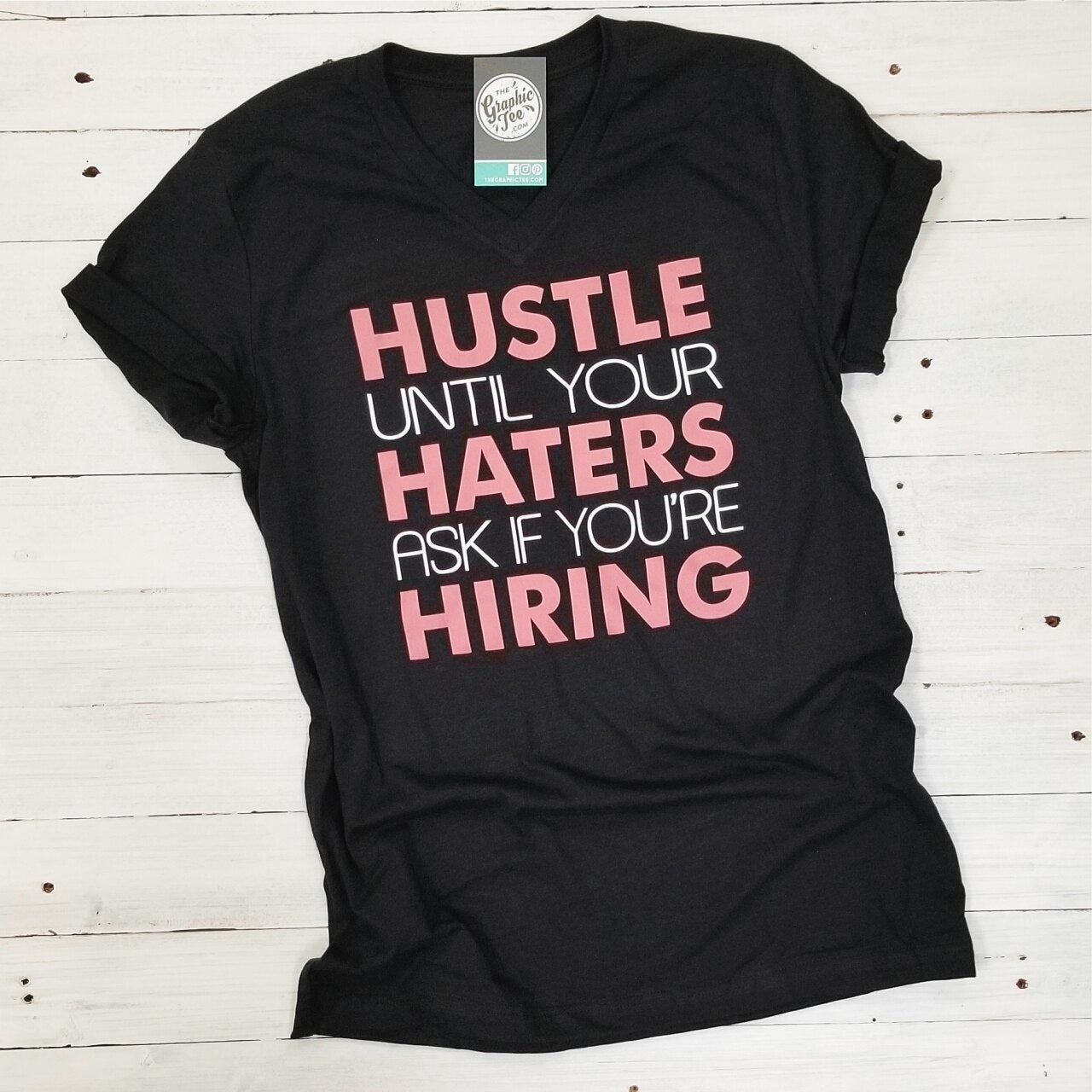 Black V-neck graphic T-shirt by The Graphic Tee with bold "Hustle Until Your Haters Ask If You're Hiring" design.