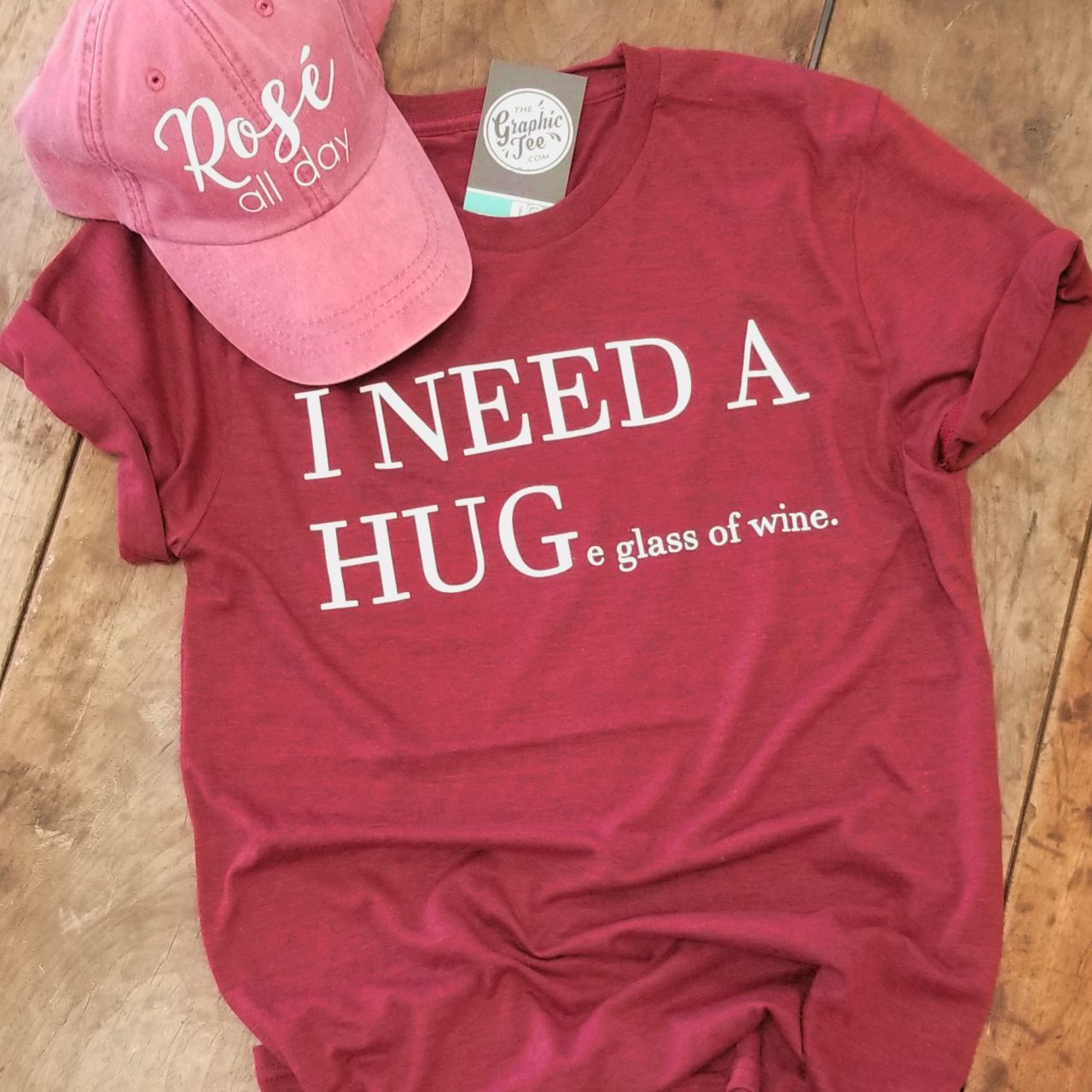 White short-sleeve graphic T-shirt featuring a humorous "I Need a HUGe glass of wine" Vino Red design by The Graphic Tee.