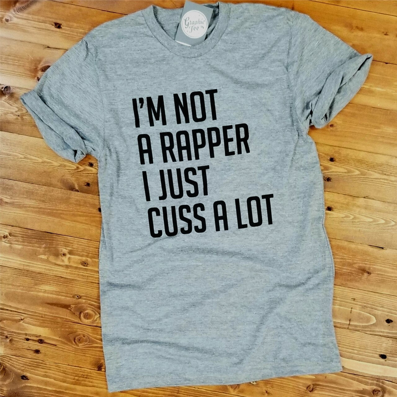 Grey unisex graphic tee from The Graphic Tee featuring the bold text "I'm Not A Rapper, I Just Cuss A Lot" on the front.