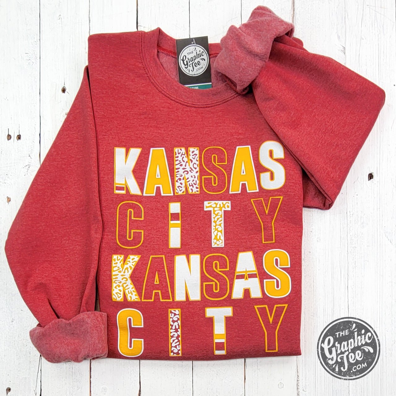 Kansas City multi-pattern letters on Heather Sport Scarlet crewneck sweatshirt by The Graphic Tee, featuring a casual, stylish design.
