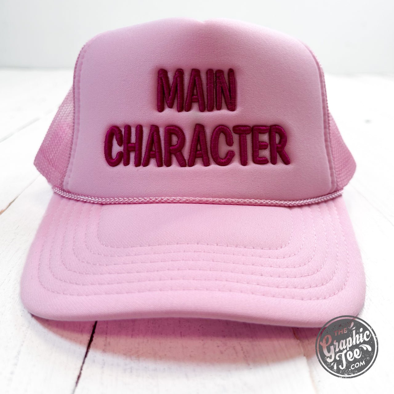Embroidered trucker cap featuring main character design by The Graphic Tee, with mesh back and adjustable strap.
