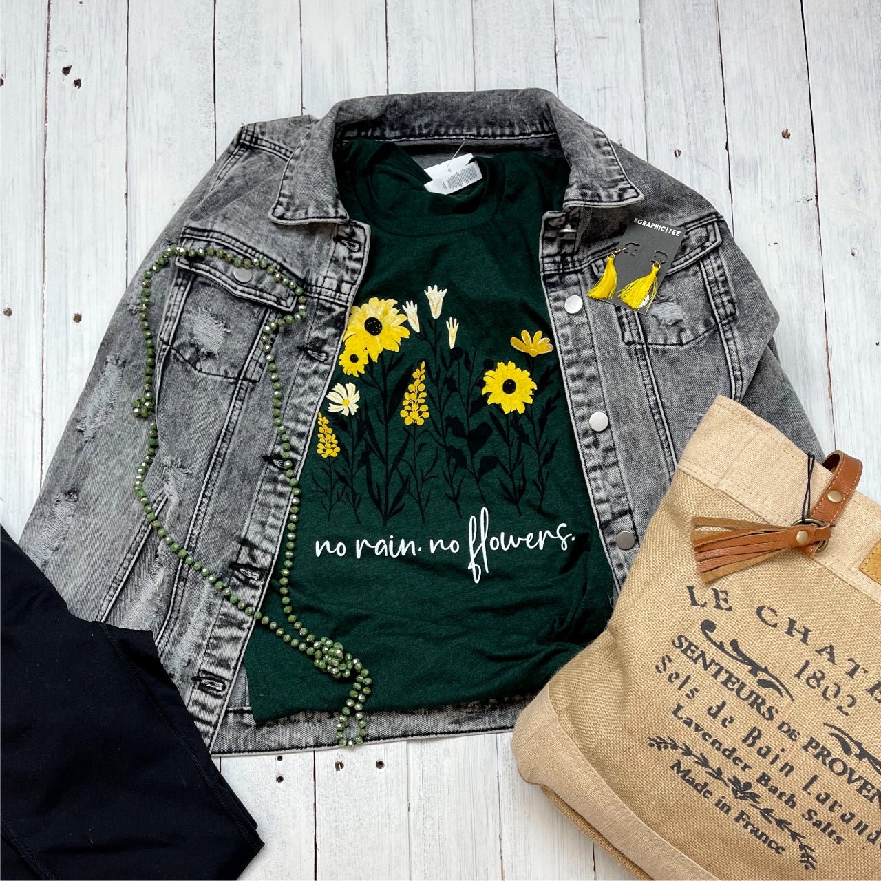 The Graphic Tee No Rain No Flowers short-sleeve graphic T-shirt with floral design on black fabric.