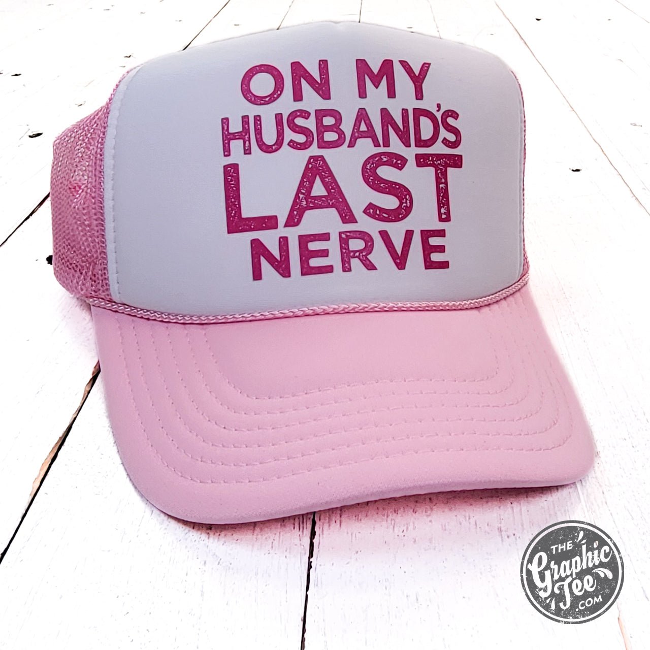 Pink and white foam trucker cap with "On My Husband's Last Nerve" slogan from The Graphic Tee, featuring mesh back and curved brim.