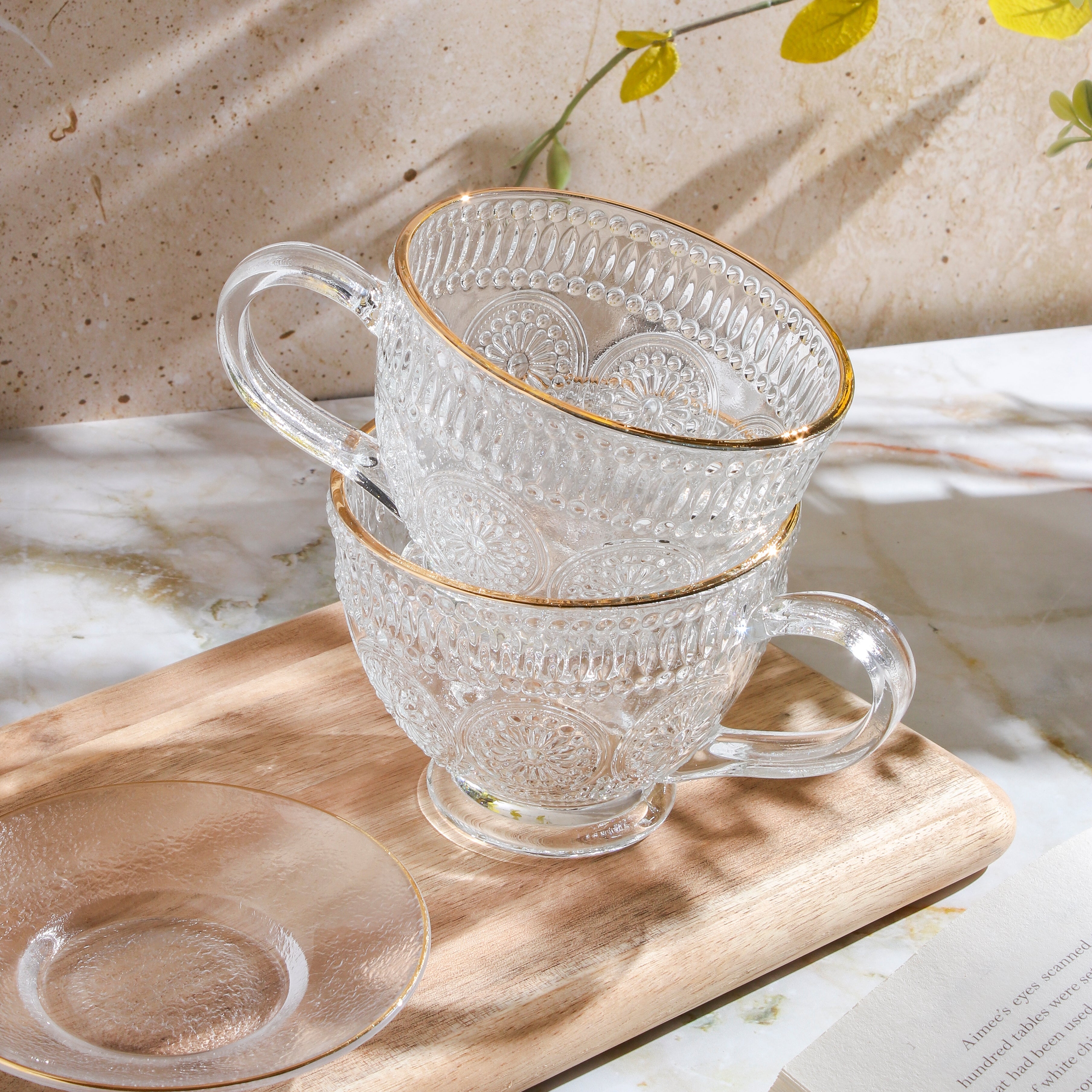 Clear glass teacup with matching saucer from Plum Deluxe Tea's Café Society collection, ideal for enjoying hot tea.