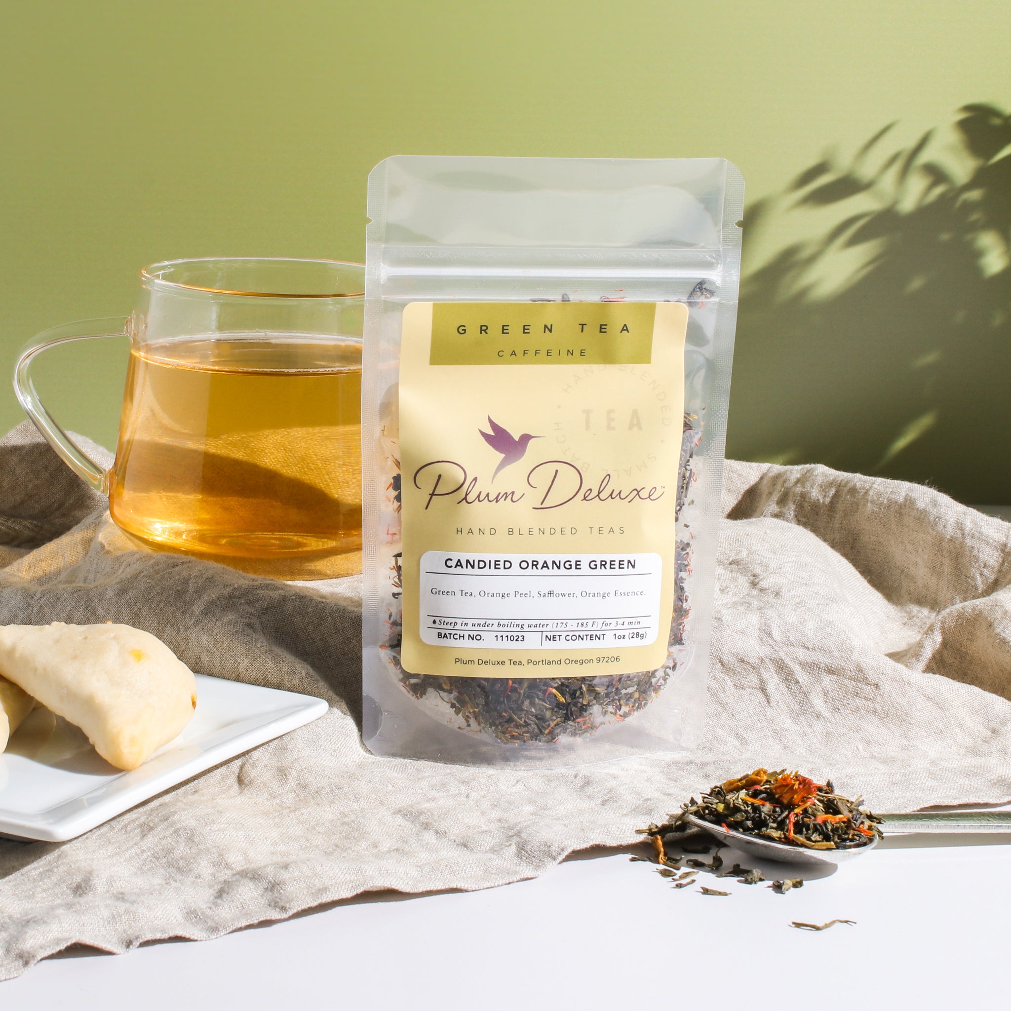 Cup of Plum Deluxe Candied Orange Green Tea with vibrant orange slices and fresh green tea leaves in a clear glass mug.