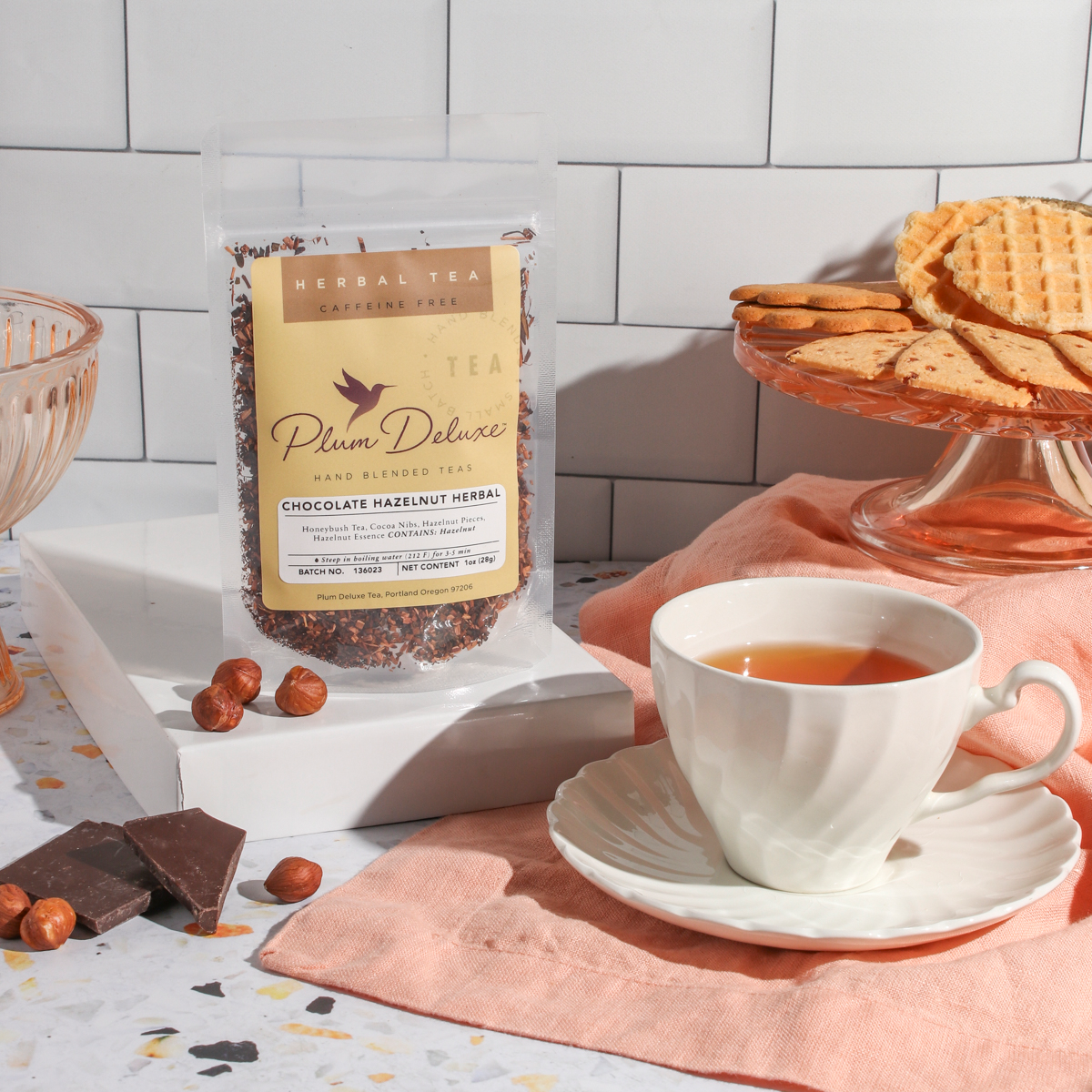 Chocolate Hazelnut Dessert Tea by Plum Deluxe Tea in a clear glass cup with brewed tea and a spoon, showcasing rich chocolate and hazelnut flavors.