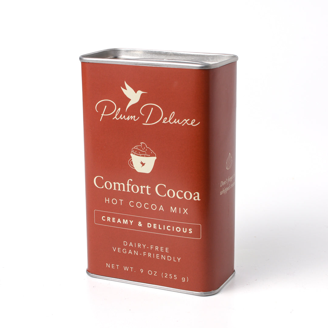 Dairy-free Comfort Cocoa Hot Cocoa Mix by Plum Deluxe Tea in a colorful package with steaming mug of hot cocoa.