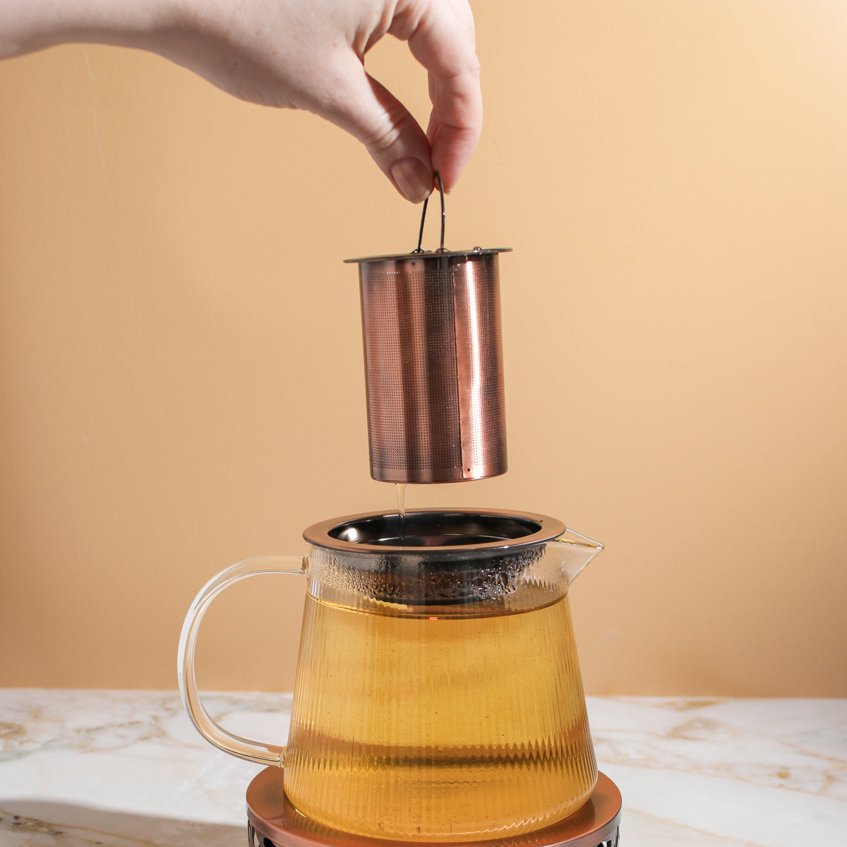 Copper rose glass teapot with teapot warmer by Plum Deluxe Tea, showcasing the elegant glass design and warm copper accents.