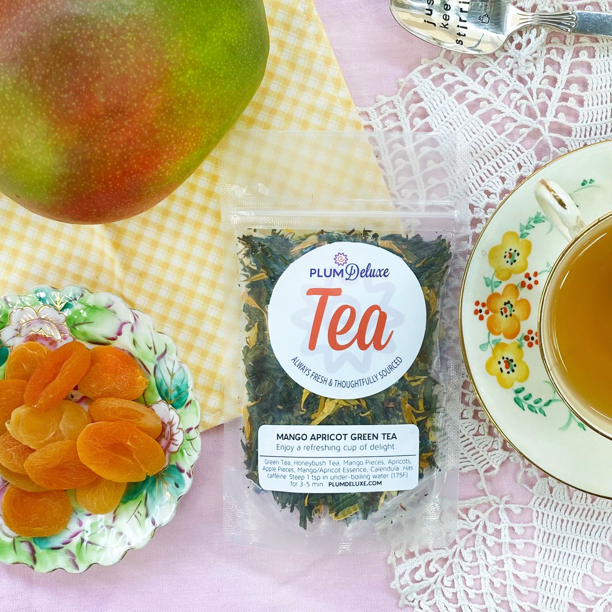 Glass cup of Plum Deluxe Mango-Apricot Green Tea with fresh fruit slices and vibrant green tea leaves.