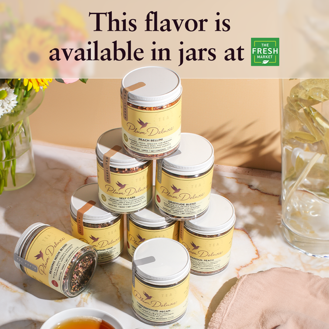 Peach Bellini Herbal Tea by Plum Deluxe Tea in a clear glass cup with fresh peach slices and herbal leaves.
