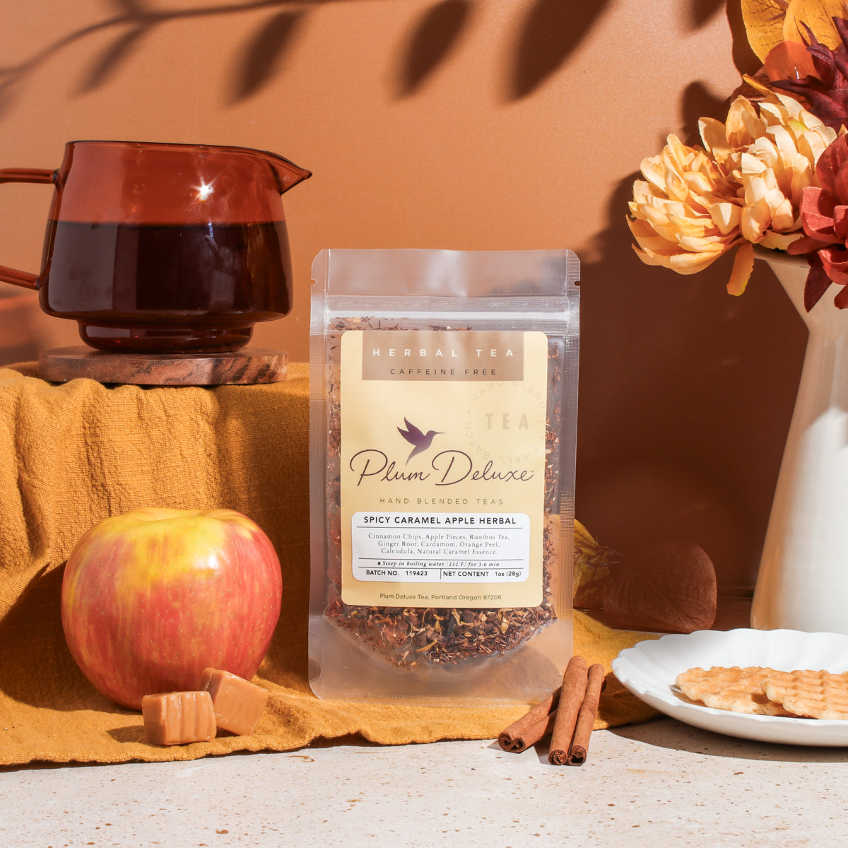 A cup of Plum Deluxe Spicy Caramel Apple Cinnamon Herbal Tea with cinnamon sticks and apple slices, steaming and ready to enjoy.