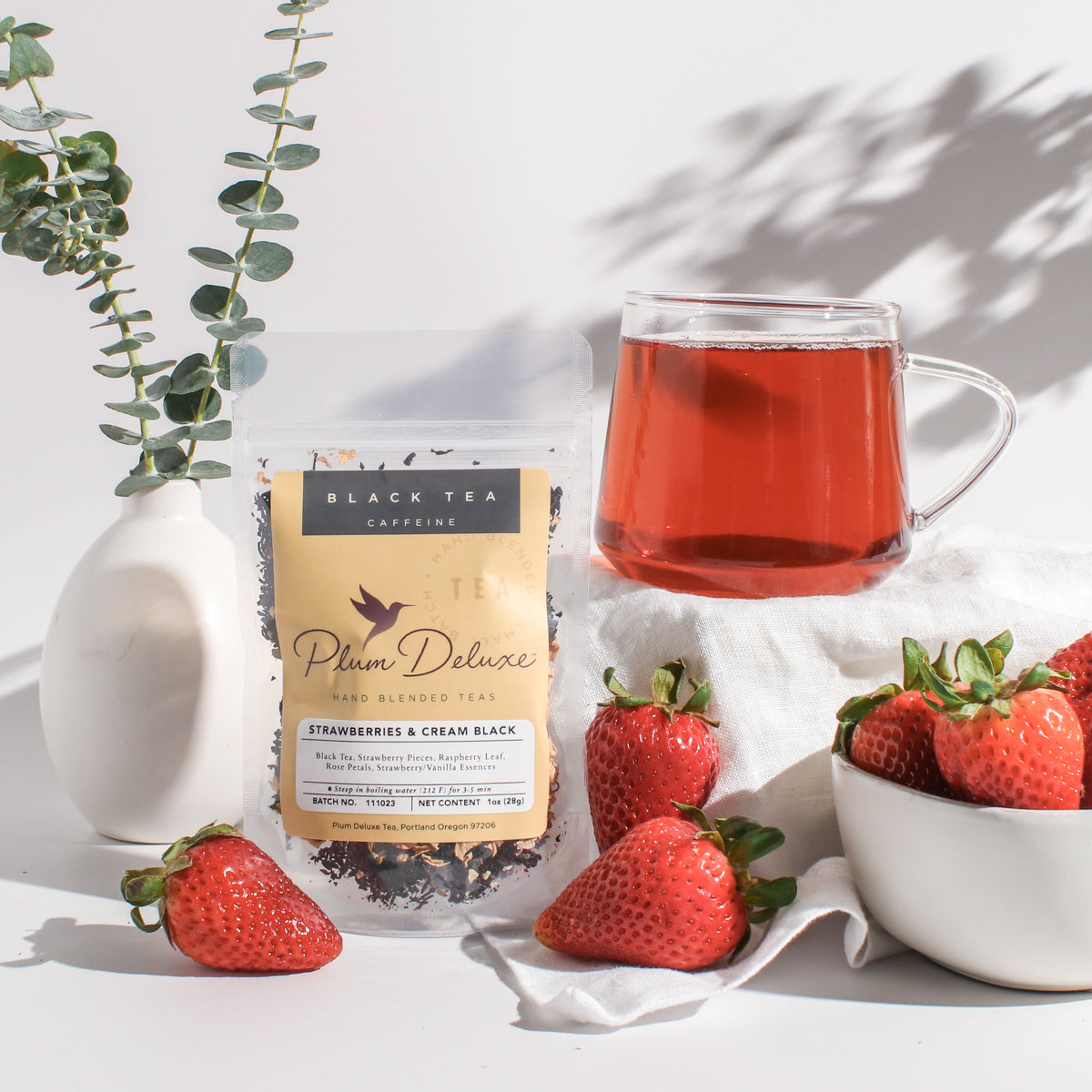 Plum Deluxe Strawberries & Cream Black Tea with Rose in a clear glass cup, showcasing brewed tea with fresh strawberry slices and rose petals.