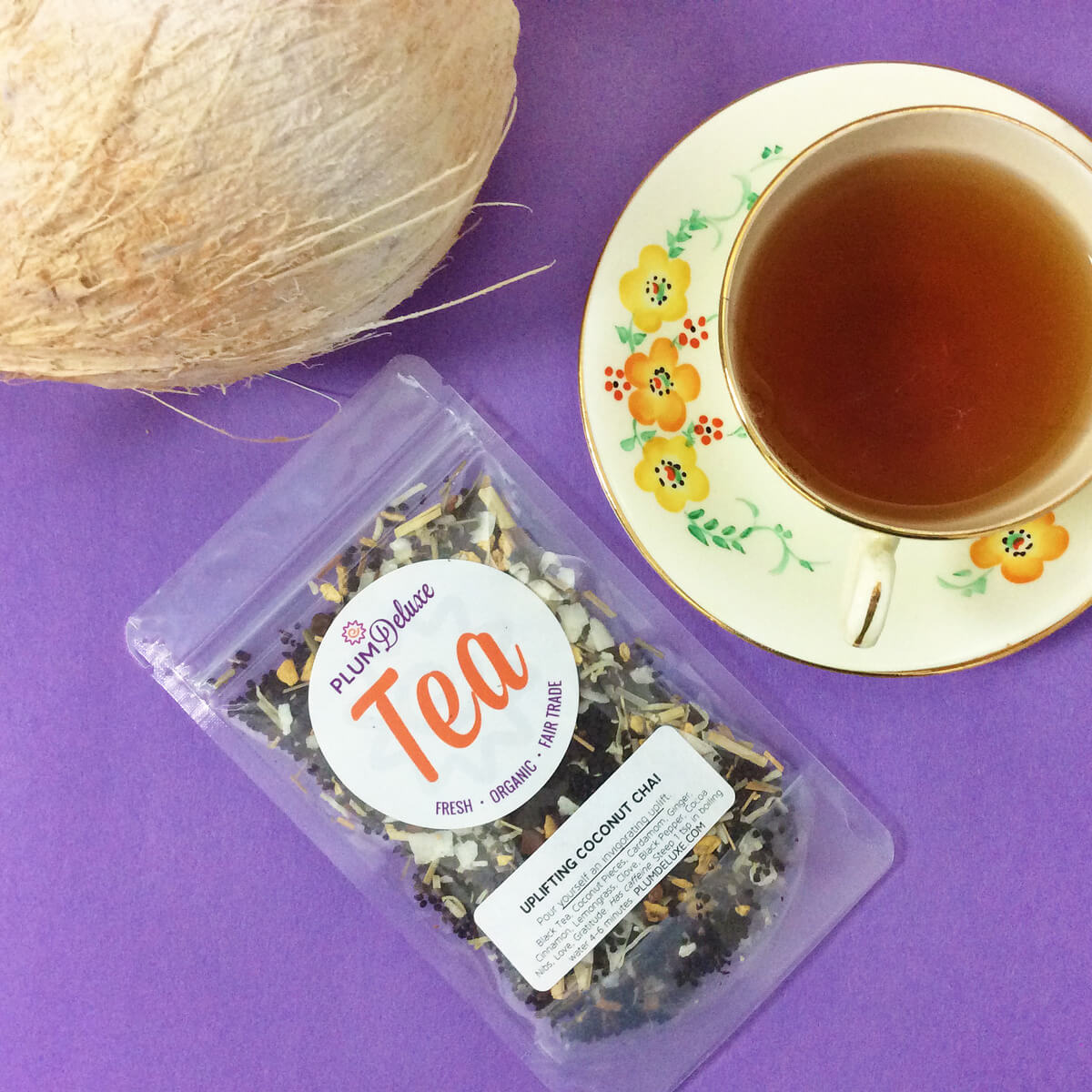 A cup of Plum Deluxe Uplifting Coconut Chai tea with coconut flakes and chai spices in a white mug on a wooden table.