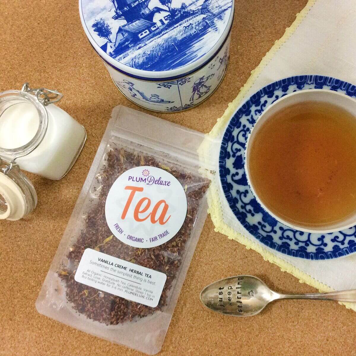 A cup of Vanilla Creme Herbal Tea by Plum Deluxe Tea with vanilla beans and herbal ingredients on a wooden table.