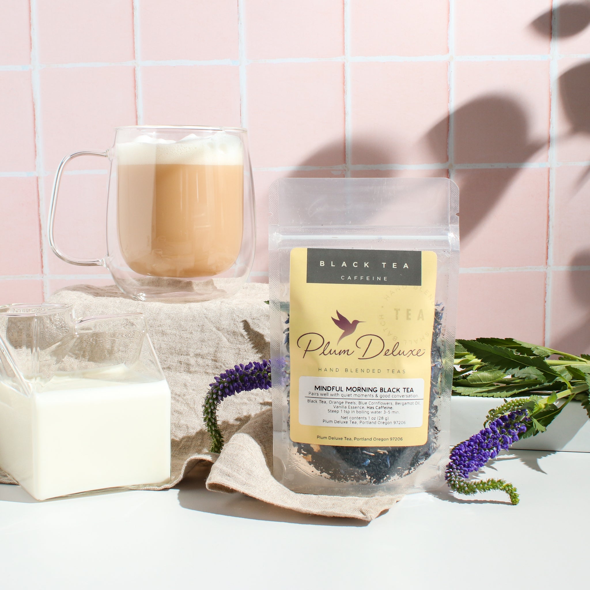 A cup of Plum Deluxe Tea's Mindful Morning Earl Grey Tea blend with loose tea leaves and a teapot on a cozy wooden table.
