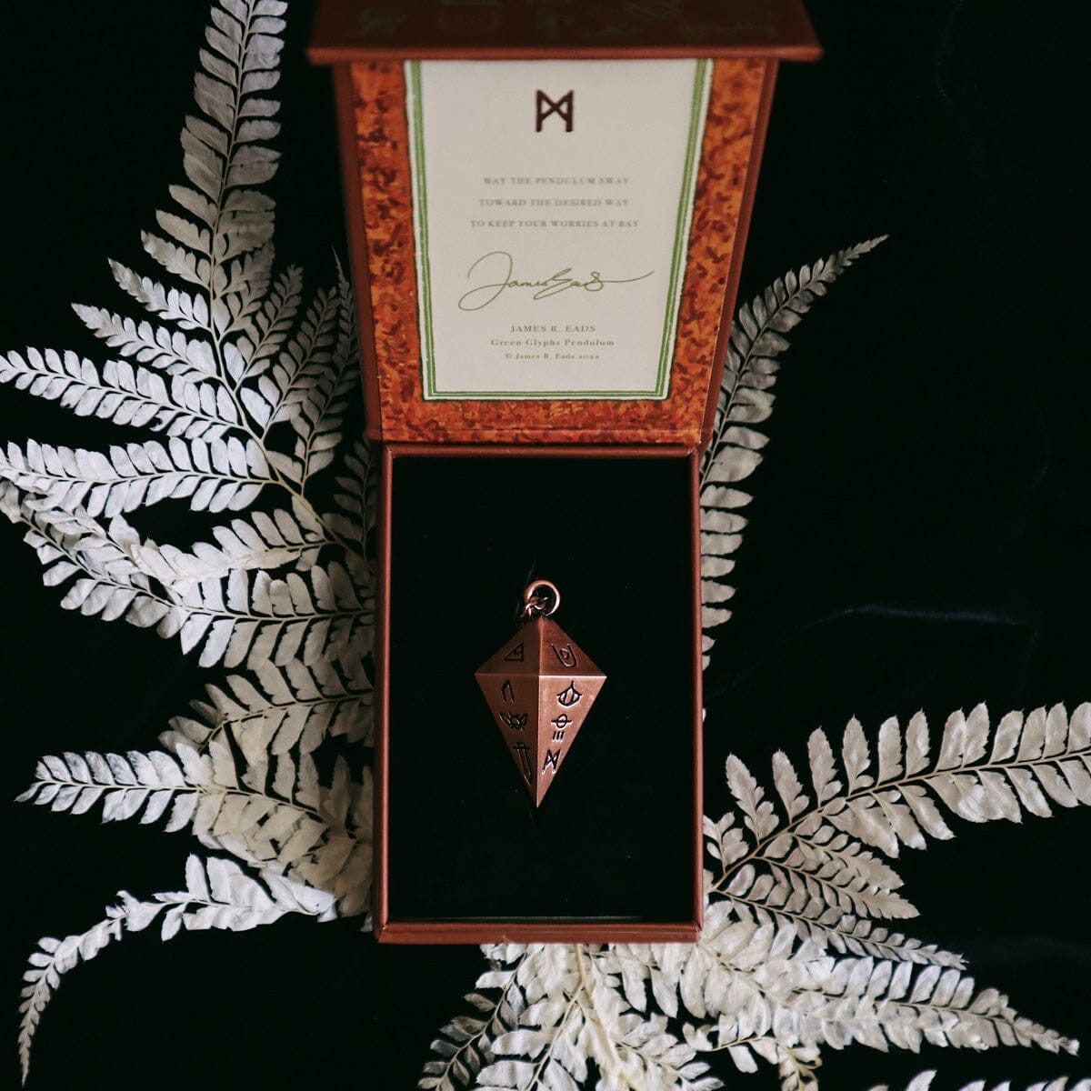 Green Glyphs Pendulum by Prisma Visions, featuring a detailed green and gold design, hanging from a chain.