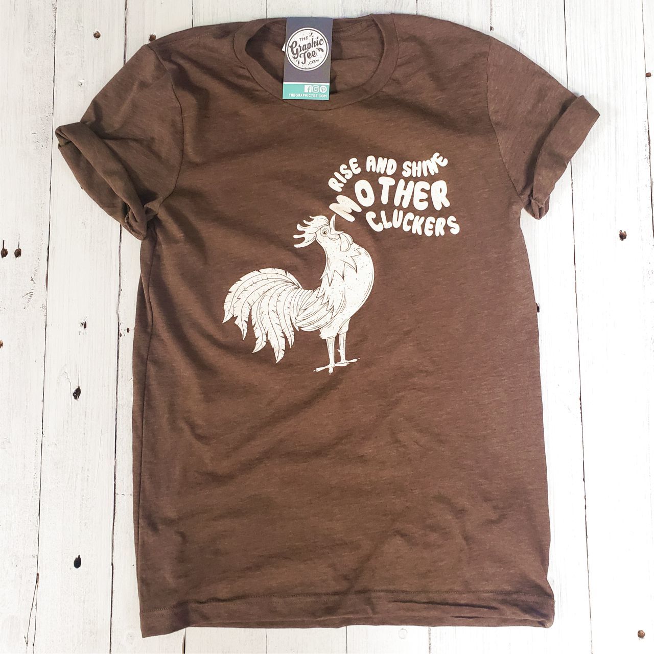 Unisex graphic tee from The Graphic Tee featuring a playful "Rise and Shine Mother Cluckers" design on soft fabric.