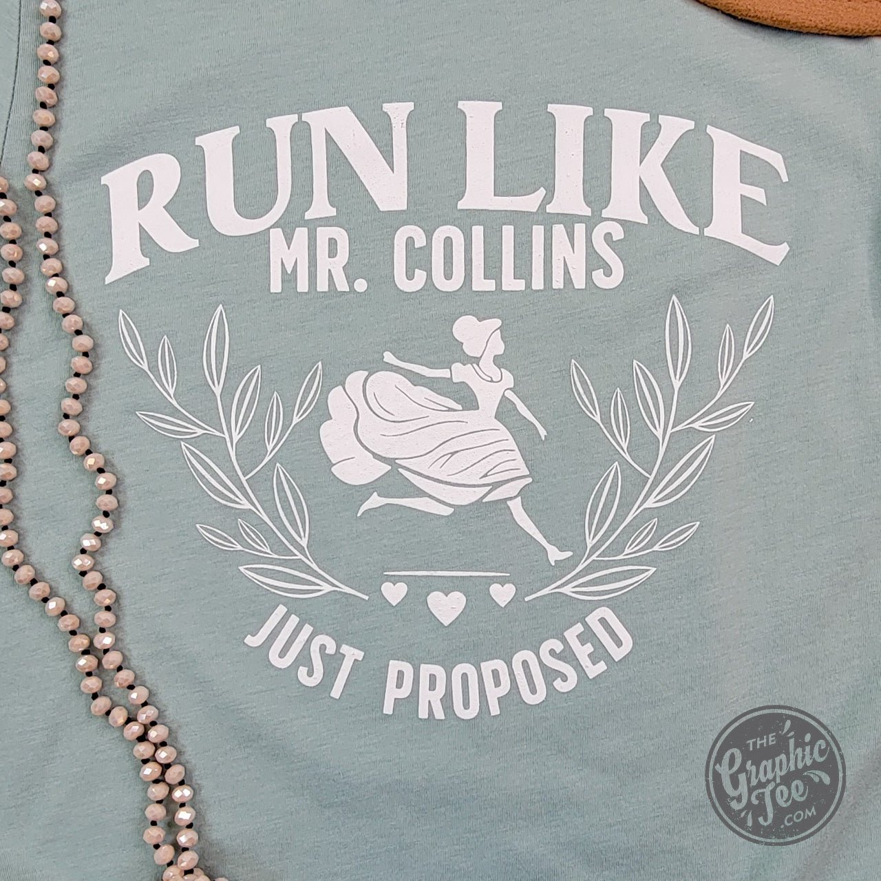 The Graphic Tee Run Like Mr. Collins Just Proposed short sleeve graphic t-shirt showing a humorous design with text and illustrations.