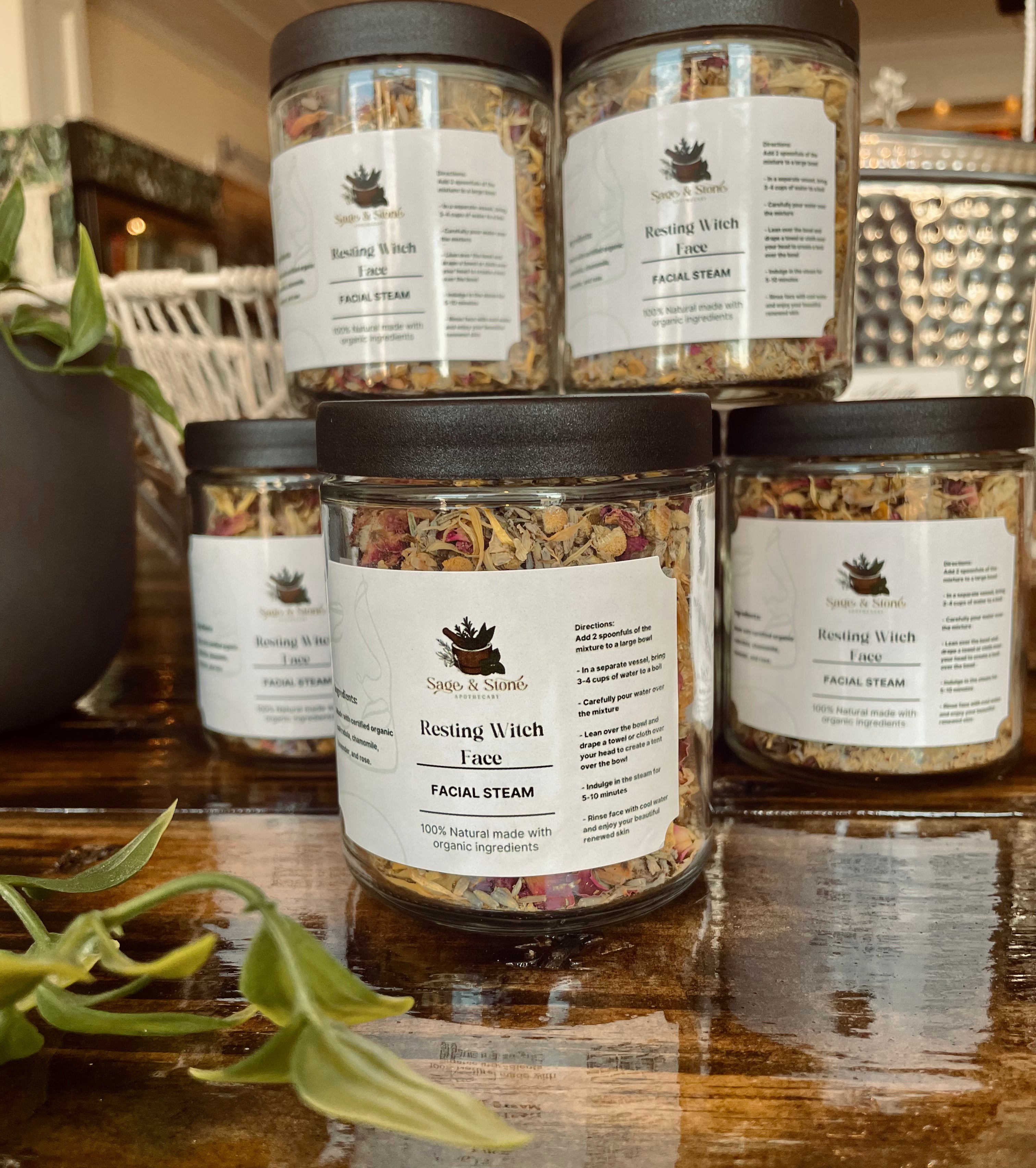 Sage & Stone Apothecary Resting Witch Face facial steam in a glass jar, surrounded by herbs and botanical ingredients for body care.