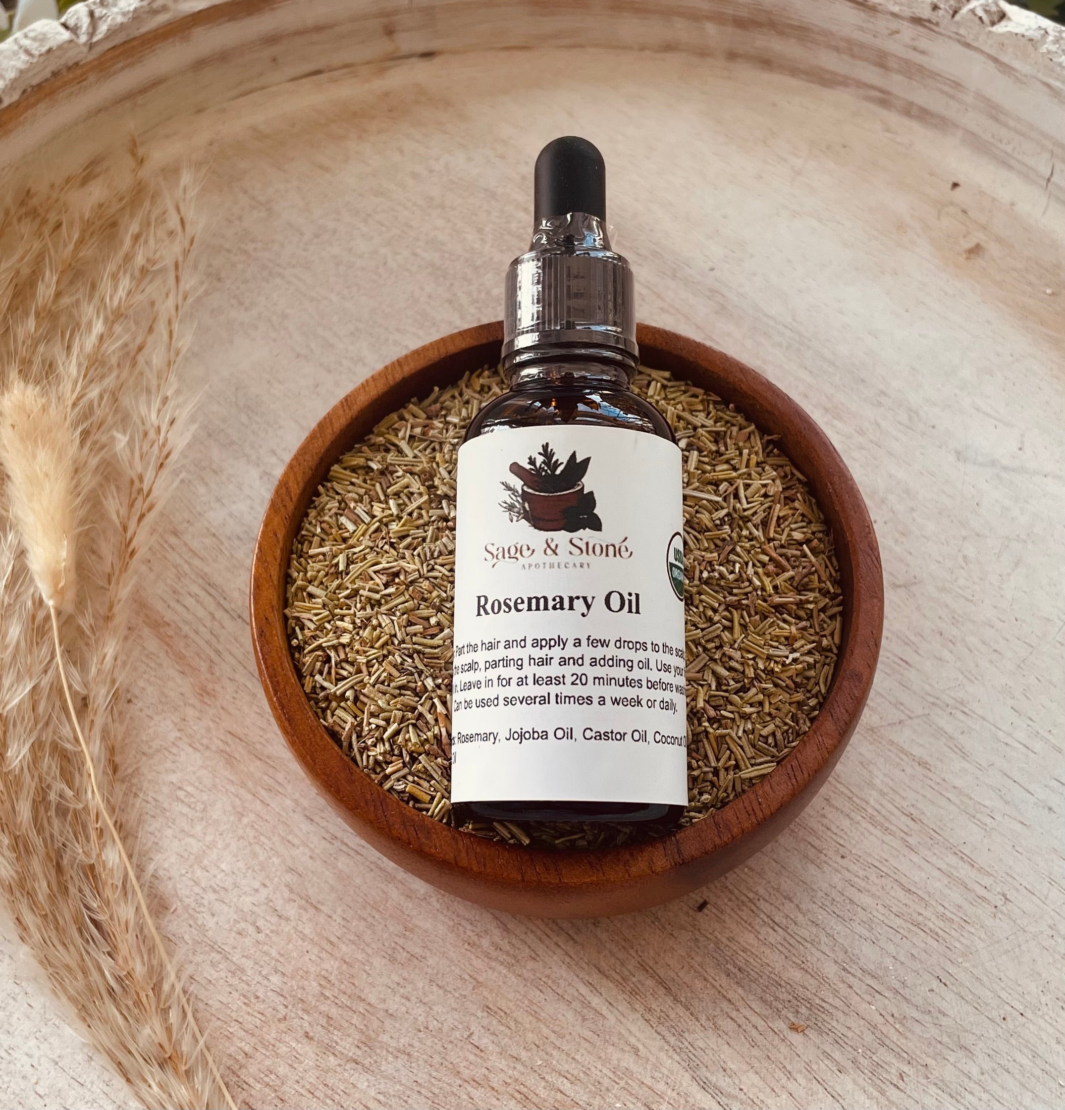 Sage & Stone Apothecary rosemary oil bottle for body care and wellness, with fresh rosemary sprigs and amber glass container.