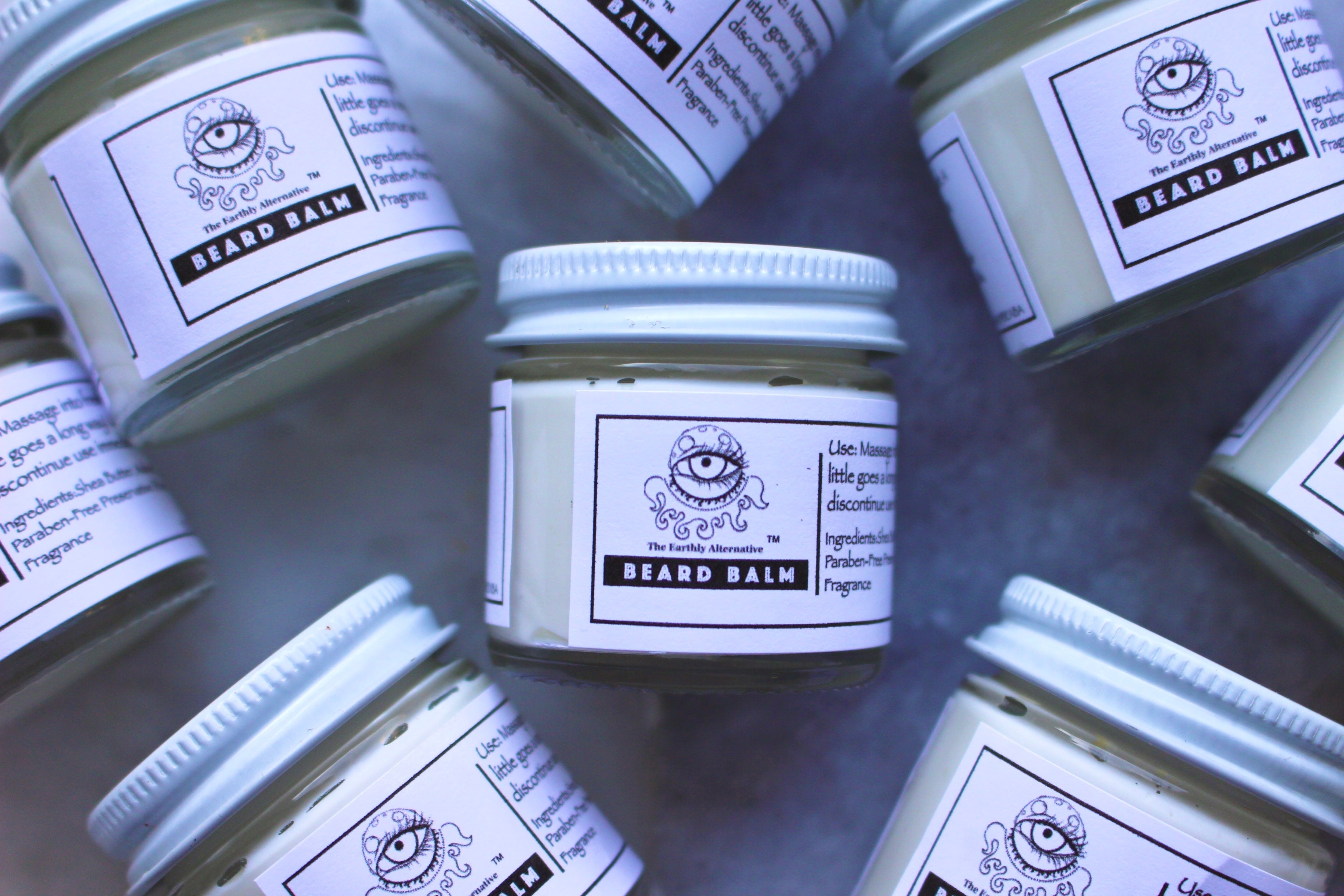 The Earthly Alternative beard balm jar with a natural label, showing a close-up of the product container and wooden background.