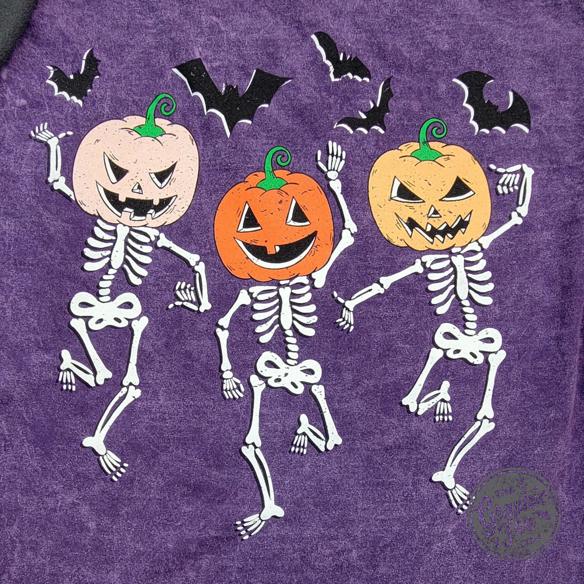 Purple Halloween short sleeve graphic tee by The Graphic Tee featuring bats and dancing skeletons front and back design.
