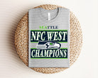 Seahawks NFC West Champions graphic tee in navy with team logo and celebratory design, worn by a person, from Anchored Grace Boutique