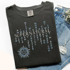 Black graphic tee featuring supernatural words design from Anchored Grace Boutique, casual apparel for fans of mystical themes.