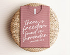 Black graphic tee from Anchored Grace Boutique featuring the quote "There is Freedom Found in Surrender" in stylish white lettering.