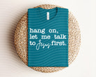Graphic tee featuring "Hang on, Let Me Talk to Jesus First" slogan, casual fit, white fabric, from Anchored Grace Boutique.