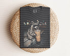 Iced coffee raccoon graphic tee from Anchored Grace Boutique, featuring a playful raccoon holding a coffee cup on soft fabric.
