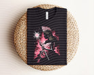 Dark graphic tee featuring a witch design from Anchored Grace Boutique, with a black fabric background and detailed witch illustration.