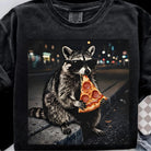 Raccoon pizza graphic tee from Anchored Grace Boutique, featuring a playful raccoon holding a slice of pizza on a casual t-shirt.